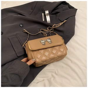 Close-up of quilted beige crossbody bag with silver bow and woven chain strap