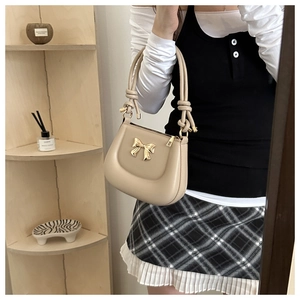 Close-up of beige crossbody bag with gold metal bow and knotted handle detail