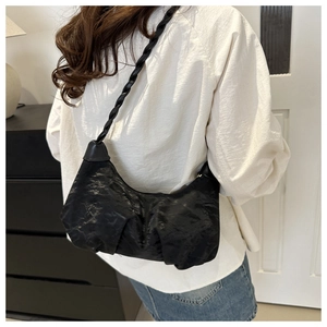 Detail of black underarm bag featuring unique ruched texture and braided leather strap