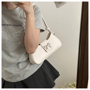 Mirror selfie showing cream baguette bag with silver bow buckle and knotted shoulder strap