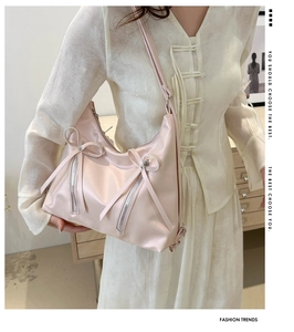 Detail of light pink shoulder bag with double bows and metal zippers shown on a model