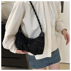 Detail of black pleated hobo bag with woven strap shown on model in a casual setting