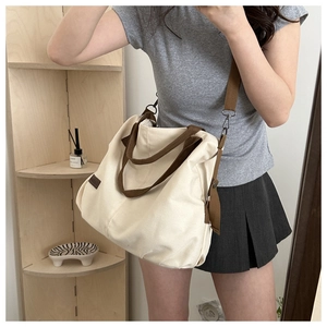 Detail view of large beige canvas tote bag with brown straps and metal hardware detail