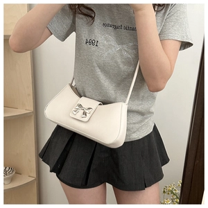 Chic cream leather baguette bag with silver bow buckle worn on a model's shoulder