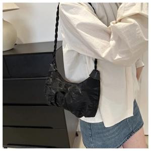 Detail of black crescent shoulder bag with pleated texture and hand-woven strap design