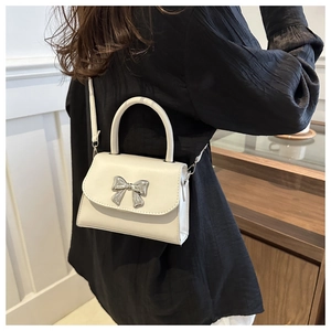 Detail of white mini crossbody bag with a silver metal bow accent worn by a model