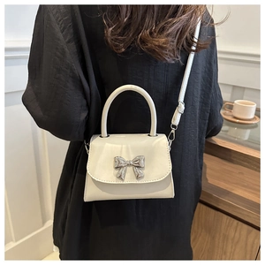 Dettaglio di una mini borsa a tracolla bianco crema con maxi fibbia a fiocco argento