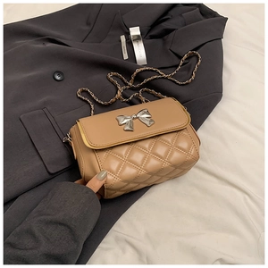 Detail of beige quilted crossbody bag featuring a silver bow and metal chain strap