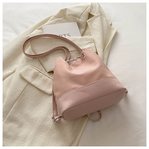 Detail of pink bucket backpack with metal chain and drawstrings against a beige blazer