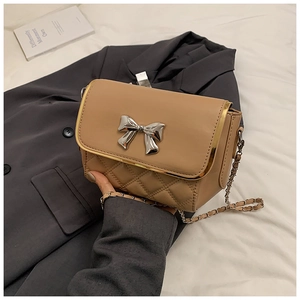 Detail of khaki crossbody bag with quilted embroidery and silver bow buckle on white linen