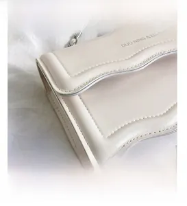 Détail du sac bandoulière en cuir crème avec bords festonnés et bandoulière chaîne