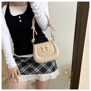 Mirror selfie showing the beige saddle bag with golden bow and unique knotted handle