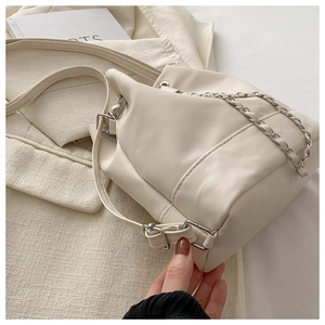 Detail of off-white bucket bag with chain strap styled on a textured cream blazer