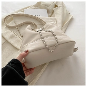 Close-up of cream white bucket bag with silver chain detail on soft white bedding