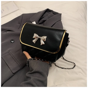 Detail of a black quilted bag with silver bow buckle and gold metal frame trim