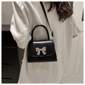 Dettaglio della mini borsa a tracolla nera con fiocco in metallo argento e texture in pelle