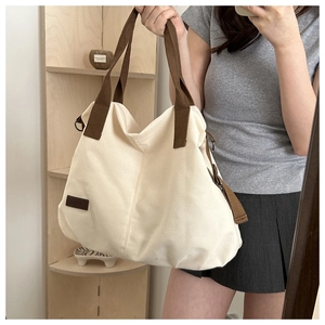Mirror selfie showing a large off-white canvas tote bag with brown handles and a logo tag