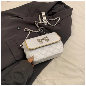Detail of white quilted crossbody bag with silver bow clasp and chain strap