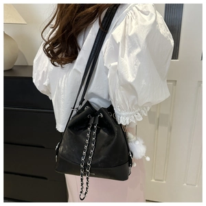 Detail showing a black leather bucket bag with silver chain drawstring and white pompom