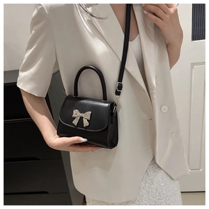Dettaglio della borsa nera con fiocco e fibbia argentata su sfondo blazer bianco