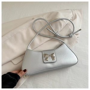 Close-up of metallic silver shoulder bag featuring a decorative metal bow and slim strap