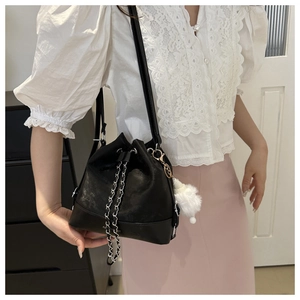Detail of black faux leather bucket bag with silver chain and white fluffy pompom charm