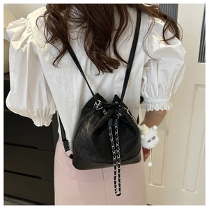 Detail of black drawstring bucket backpack with metal chain and plush charm on female model