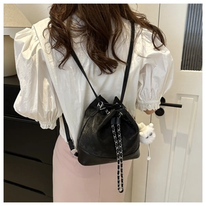 Detailed view of black leather bucket backpack with chain drawstring and plush bear charm