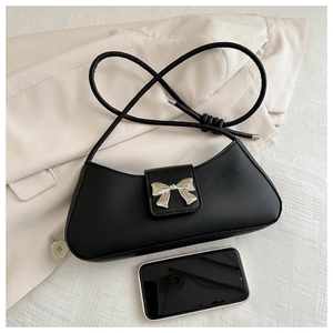 Close-up of black shoulder bag featuring a silver bow buckle on cream blazer