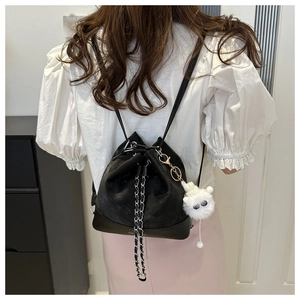 Detail of black drawstring bucket backpack with chain strap and plush monster charm