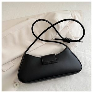 Close-up of black leather baguette bag with knotted strap on a white blazer