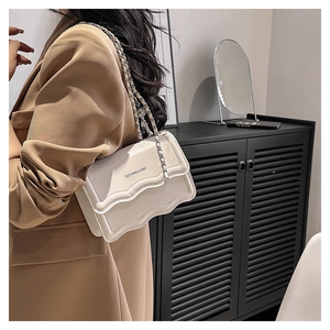 Gros plan d'un petit sac bandoulière blanc avec bordure ondulée et chaîne dorée chic
