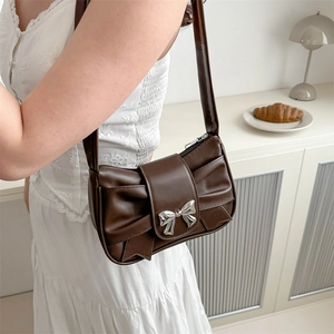 Sac sous le bras plissé marron avec boucle nœud argenté sur modèle en robe blanche