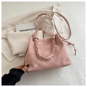 Dettaglio borsa hobo rosa con manico intrecciato e trama marmorea su abito beige