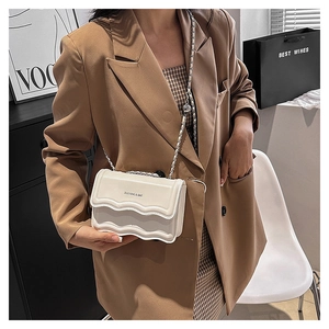 Détail du sac à bandoulière blanc cassé élégant avec rabat ondulé et bandoulière chaîne