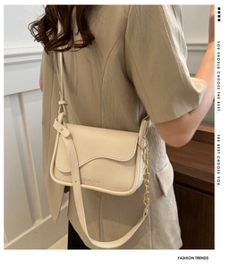Detail of cream crossbody bag featuring a wavy flap design and gold chain strap