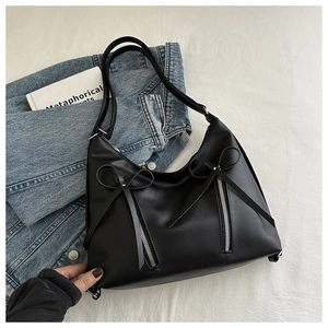 Détail d'un sac hobo noir avec fermetures éclair argentées et nœuds sur tissu blanc cassé