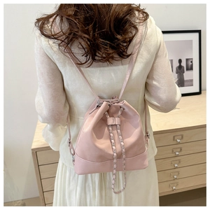 Rear view of a model wearing a soft pink drawstring bucket backpack with silver chain