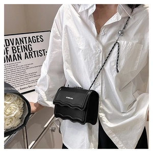 Détail d'un sac bandoulière noir avec rabat ondulé et chaîne porté par un mannequin