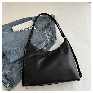 Détail du sac hobo noir minimaliste en similicuir mat sur fond de veste en jean