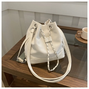 Detailed view of white bucket bag with drawstring closure and silver chain on a table
