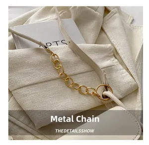 Detail shot of a cream white saddle bag showing the gold chunky metal chain connection