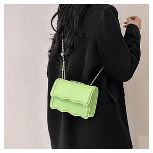 Détail du sac à bandoulière vert aux bords festonnés et chaîne argentée sur blazer noir