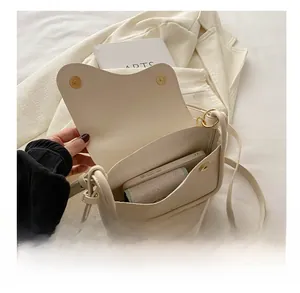 Detail of minimalist cream leather crossbody bag interior holding a smartphone