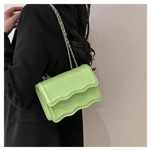 Détail du sac bandoulière vert citron avec bord ondulé et chaîne argentée sur blazer