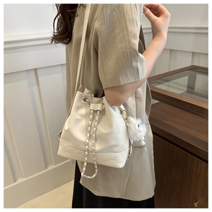 Detailed view of white bucket bag with chain drawstring and plush ball charm