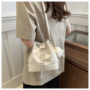 White bucket bag with chain drawstring and plush pom-pom charm shown in a cozy room