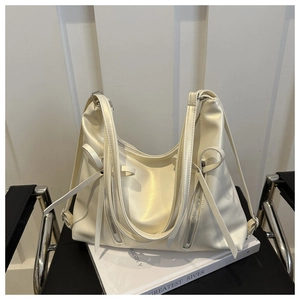 Détail du sac à bandoulière en cuir crème avec fermetures éclair et ruban sur un livre