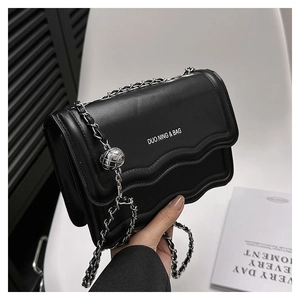 Gros plan d'un sac en cuir noir avec rabat festonné et pendentif sphérique argenté