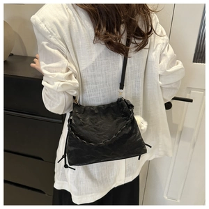 Dettaglio borsa tote in pelle nera a pieghe con tracolla intrecciata e pompon bianco